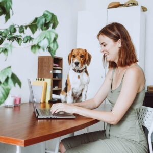 person typing on laptop next to dog