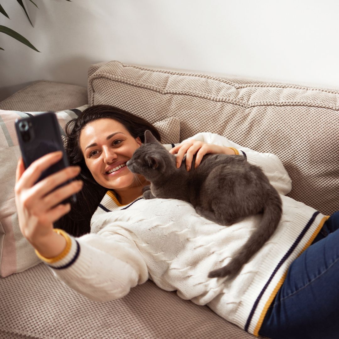 Person lying on a couch and taking a selfie with a cat
