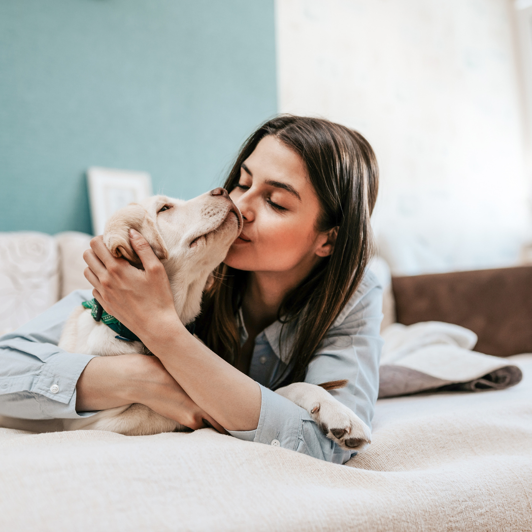A woman kissing her dog on her bed