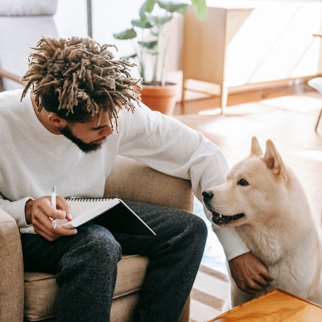 a pet sitting petting a dog and writing in a notebook