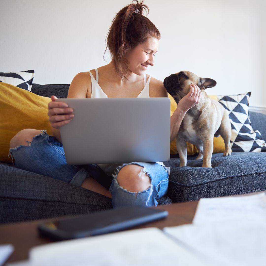 a woman petting her dog on the couch while she is on a laptop