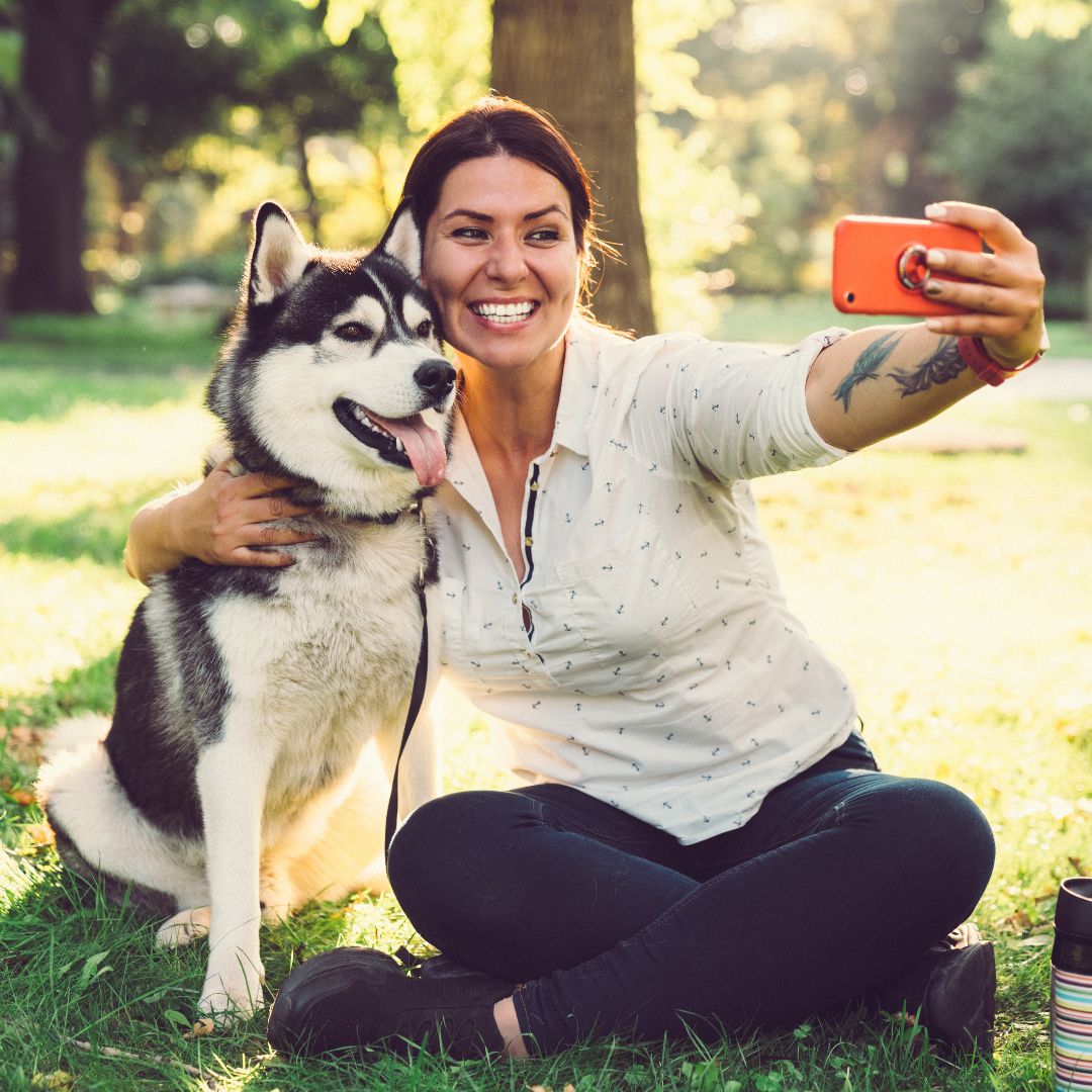 a person taking a selfie with a husky on a leash outside